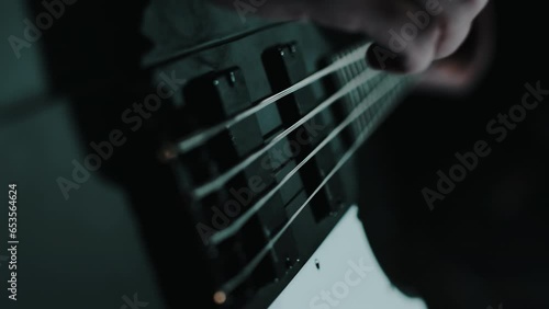 A close-up of a rock musician playing an electric guitar passionately and quickly, plucking strings, illuminated by cold light in a studio