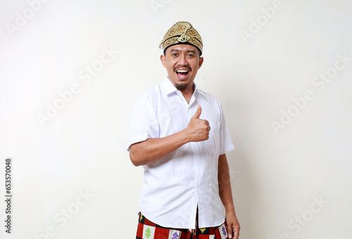 Happy Asian man in balinese traditional costume standing while showing thumbs up. Isolated on white background