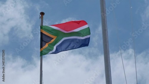 South African flag blowing in the wind on a flag pole with a blue sky and clouds