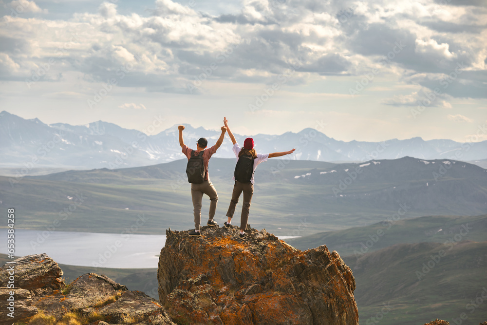 Obraz premium Young couple of hikers with backpacks are standing at mountain top with open arms in winner pose