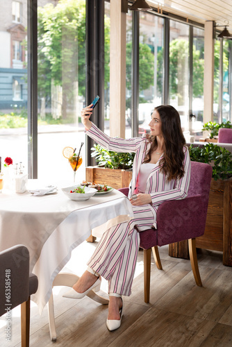 brunette girl has dinner, lunch in a restaurant. eats salad and cocktail, girl waits for friends in restaurant © Kateryna Muzhevska