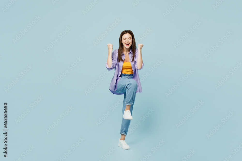 Full body young happy woman she wears purple shirt yellow t-shirt casual clothes doing winner gesture celebrate clenching fists say yes isolated on plain pastel light blue background studio portrait. Full body young happy woman she wears purple shirt yellow t-shirt casual clothes doing winner gesture celebrate clenching fists say yes isolated on plain pastel light blue background studio portrait.