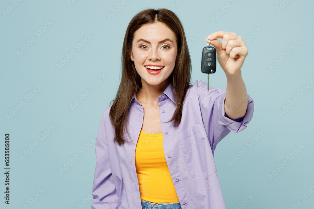 Young happy shocked excited woman wears purple shirt yellow t-shirt casual clothes hold car keys fob keyless system isolated on plain pastel light blue background studio portrait. Lifestyle concept. Young happy shocked excited woman wears purple shirt yellow t-shirt casual clothes hold car keys fob keyless system isolated on plain pastel light blue background studio portrait. Lifestyle concept.