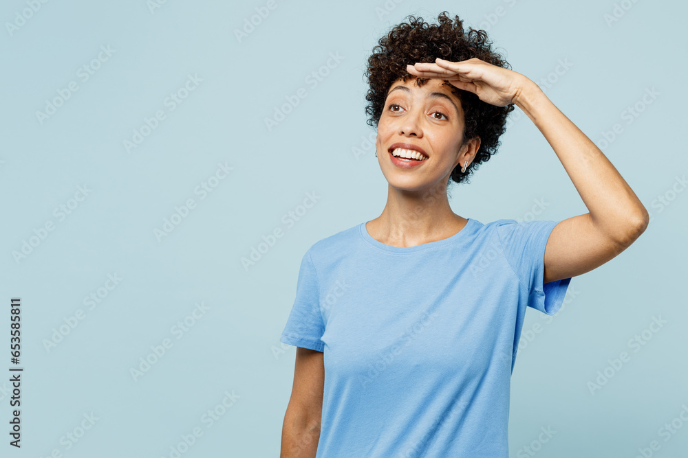 Young happy woman of African American ethnicity wear t-shirt casual clothes hold hand at forehead look far away distance isolated on plain pastel light blue cyan background studio. Lifestyle concept. Young happy woman of African American ethnicity wear t-shirt casual clothes hold hand at forehead look far away distance isolated on plain pastel light blue cyan background studio. Lifestyle concept.