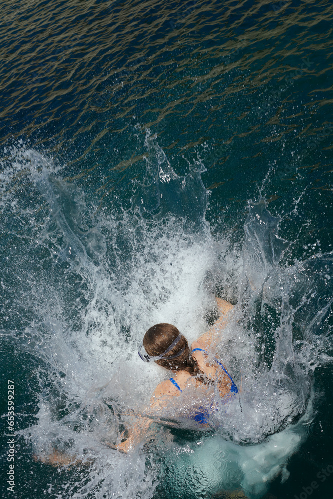 a woman jumps into the sea, creating splashes around her. View from above