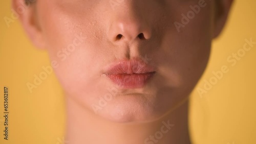 Extreme close up of woman lips making skeptical or superior gestures with her lip and puffing her cheeks against a yellow background in slow motion