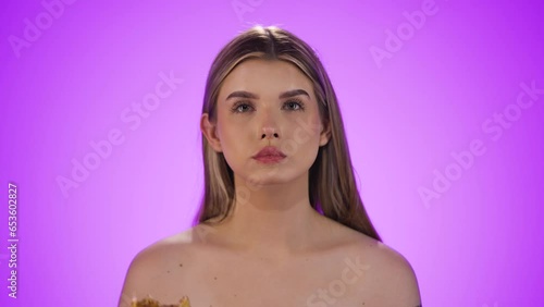 Medium shot of an attractive young woman happily biting into a slice of delicious vegan pizza while rejoicing and satisfying her hunger in front of purple background in slow motion