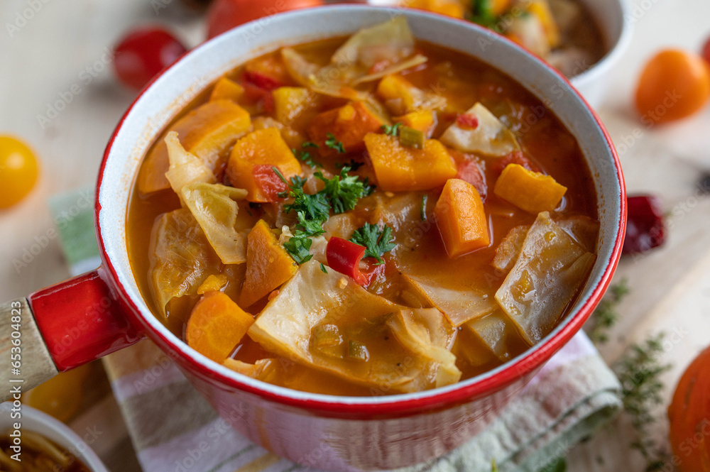 Cabbage soup with pumpkin, carrots and tomatoes in a red pot Cabbage soup with pumpkin, carrots and tomatoes in a red pot