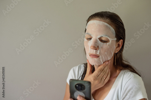 Wallpaper Mural woman with a fabric cosmetic mask on her face, does skin care. Close-up portrait on a gray background. beauty industry, self-care. Torontodigital.ca
