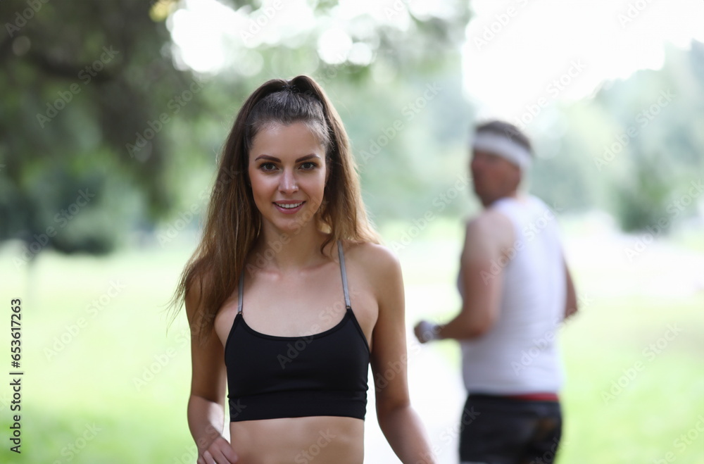 Portrait of beautiful fit female posing on camera outdoors. Morning park run for strong body. Man watching pretty girl from back. Sport and active lifestyle concept Portrait of beautiful fit female posing on camera outdoors. Morning park run for strong body. Man watching pretty girl from back. Sport and active lifestyle concept