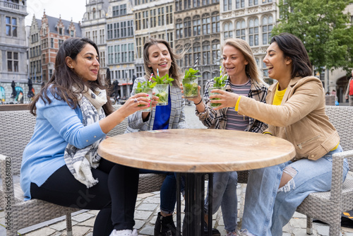 Canvas Print A lively image featuring a multi-ethnic group of female friends savoring refreshing Mojito cocktails on a cafe terrace located in a bustling European city center