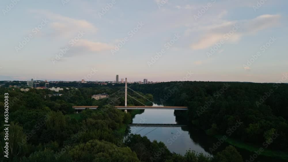 The camera flies along the river to the pedestrian bridge. Drone flying over the park The camera flies along the river to the pedestrian bridge. Drone flying over the park
