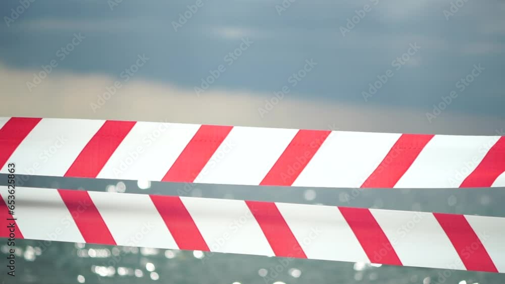 Red white warning tape barrier ribbon swinging in the wind across exotic sea beach background without people. No entry Red White caution tape. No holiday concept, delayed travel, no summer plans Red white warning tape barrier ribbon swinging in the wind across exotic sea beach background without people. No entry Red White caution tape. No holiday concept, delayed travel, no summer plans