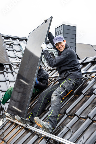 Smiling technician during installation of a solar panel on the roof of a house © photoschmidt