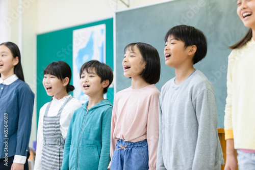 黒板の前で歌を歌う小学生たち photo