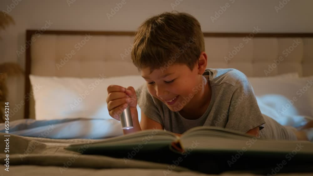 Smiling happy little cute caucasian child kid boy schoolboy reading interesting book evening in bedroom holding flashlight lying on bed at home read fairytale story for night bedtime enjoying learning Smiling happy little cute caucasian child kid boy schoolboy reading interesting book evening in bedroom holding flashlight lying on bed at home read fairytale story for night bedtime enjoying learning