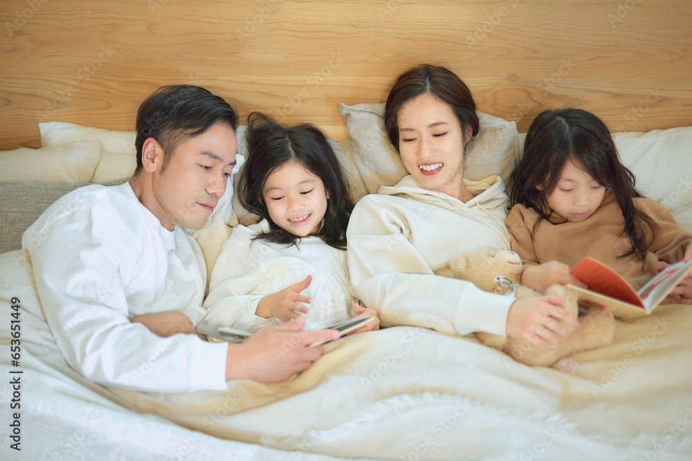 寝室で本を読み聞かせる家族 寝室で本を読み聞かせる家族