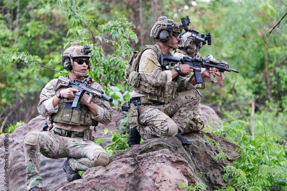 Fototapeta premium Military army soldiers tactical team, commando group moving cautiously in forest area, kneeling and looking around, covering comrades, controlling sectors. Commander showing halt or stop hand signal