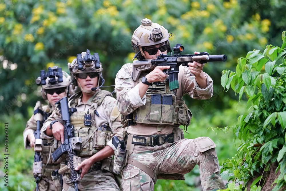 Fototapeta premium Military army soldiers tactical team, commando group moving cautiously in forest area, kneeling and looking around, covering comrades, controlling sectors. Commander showing halt or stop hand signal