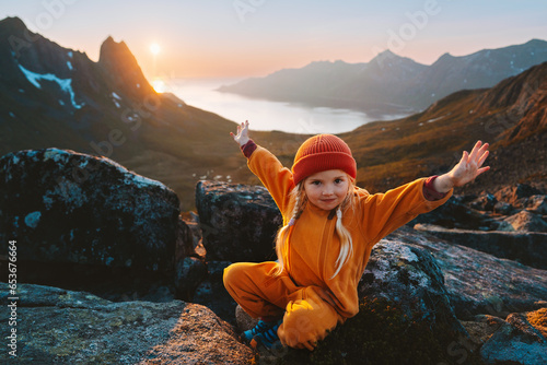 Child girl hiking in mountains travel vacations in Norway adventure outdoor active healthy lifestyle 4 years old kid happy raised hands enjoying midnight sun landscape photo