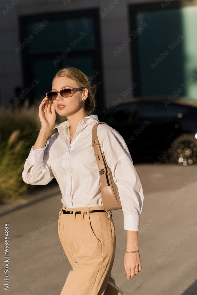 Fototapeta premium Portrait of a young and attractive Caucasian woman in casual clothes and sunglasses while walking around the city. The concept of fashion, style, youth and lifestyle