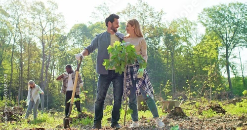 Delightful couple working together during forestation work. Beautiful Caucasian man and cute young woman planting trees with other volunteers. Helping nature and environment.