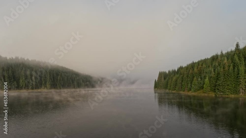 Aerial flying view of early morning mist floating over calm water lake. Slowly floating vapor, water evaporating over lake at down time, before sunrise 