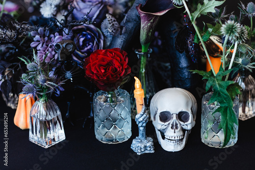 Halloween table arrangement with skull, candle, red and blue roses and thorny plants in a dark colour scheme.