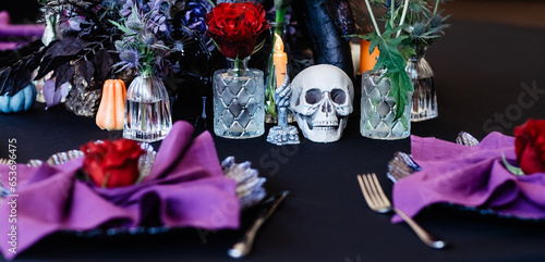 Festive Halloween table setting in black, purple and red colours with roses, skull and prickly plants.