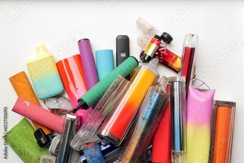 A vibrant collection of discarded electronic cigarette vapes and internal components shot over a white plastic background.
