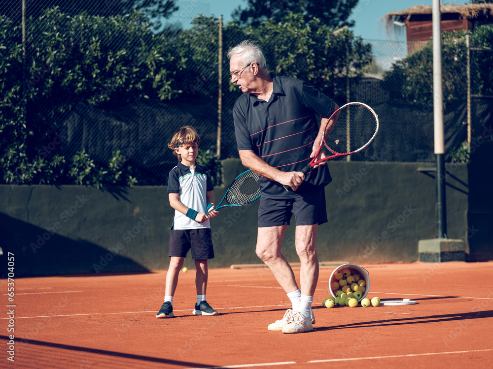 Senior tennis instructor teaching preteen boy on hard court