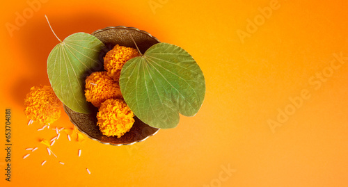 Dussehra greeting card photo background with clear space for message. Top view of a Dussehra leaves and marigold flower in a bowl on saffron color background. photo