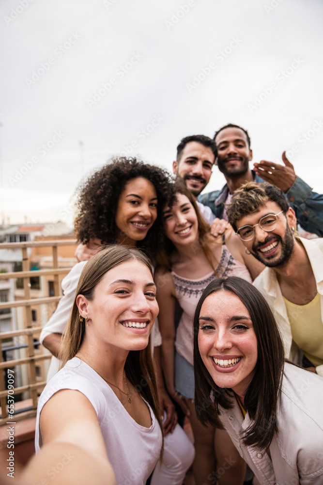 Fototapeta premium Multicultural cheerful group of carefree friends taking a selfie in a rooftop party.Multiracial beautiful young happy people smiling while taking a picture in a terrace.