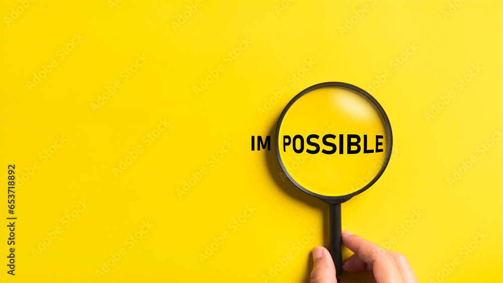 Hand holding magnifying glass with possible and impossible words on the yellow background. Optimistic and Business metaphor concept. - obrazy, fototapety, plakaty 