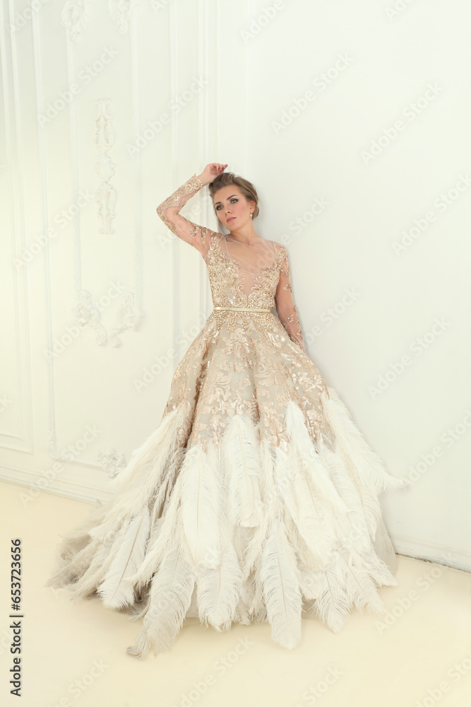 Fototapeta premium Fashion portrait of sensual fashionable model woman wearing white and gold evening gown in white interior