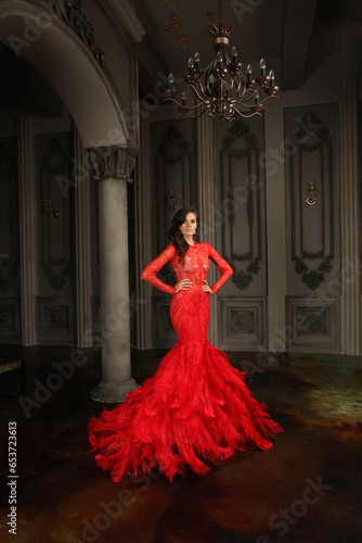 Beautiful sensual glamourous brunette model in red evening gown standing in vintage interior