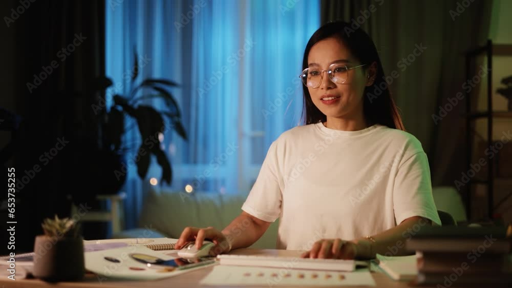Excited young asian woman gamer sitting at desk and playing in video games on computer at home Happy player female take part in online competition at late night Excited young asian woman gamer sitting at desk and playing in video games on computer at home Happy player female take part in online competition at late night