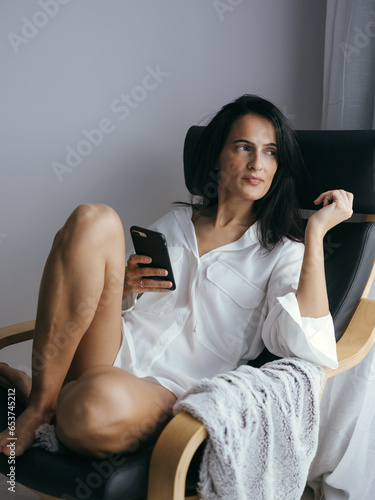 Canvas Print Feminine ethnic lady relaxing in armchair with smartphone in han
