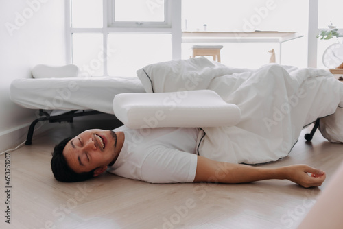 Asian man sleeping lying on floor, having good dream, fall from white bed at home.