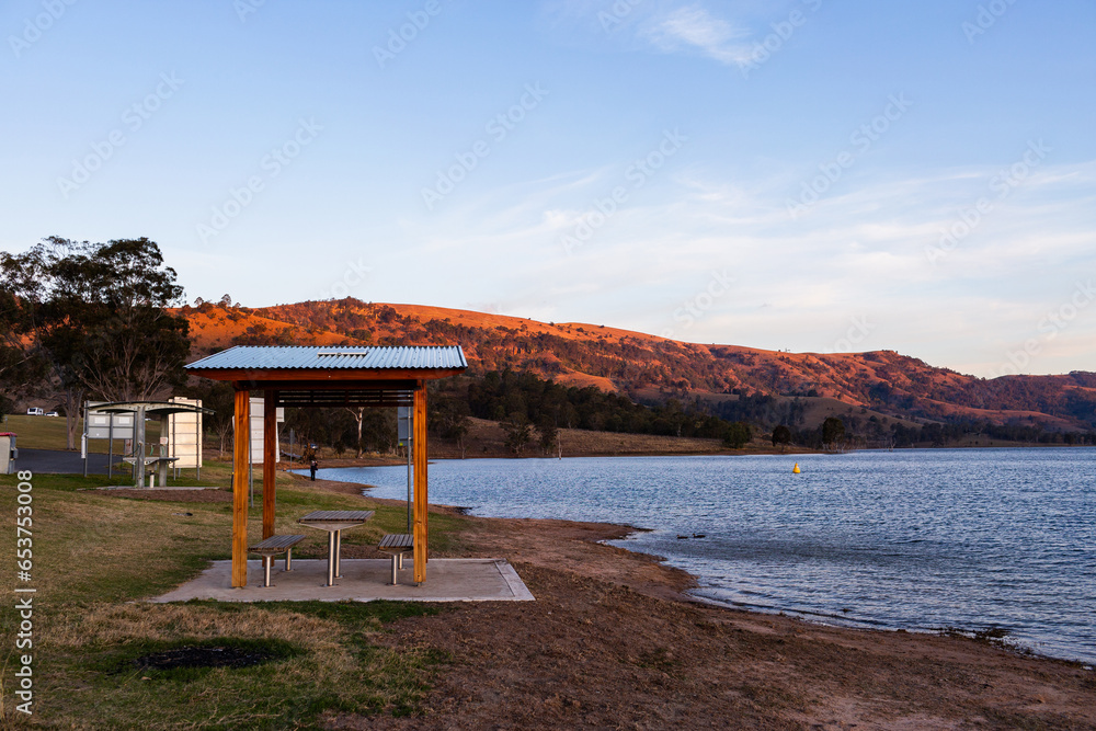 Last light of day on hills behind lakeside picnic shelter and bench Last light of day on hills behind lakeside picnic shelter and bench