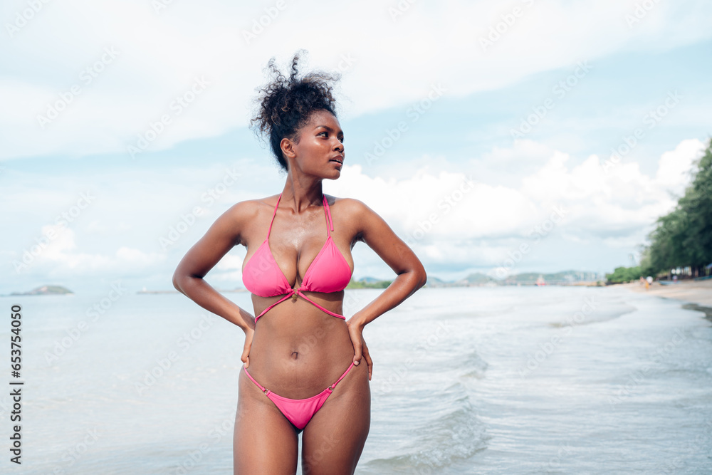 Beautiful African american woman in pink bikini on tropical beach. Portrait of dark skinned woman smiling at sea. Brunette tanned girl in swimwear enjoying and walking on beach. Beautiful African american woman in pink bikini on tropical beach. Portrait of dark skinned woman smiling at sea. Brunette tanned girl in swimwear enjoying and walking on beach.