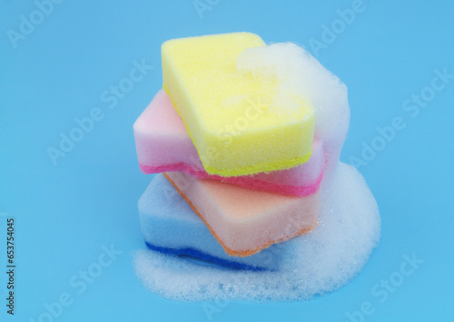 Stack of many sponges with soap foam on blue background. Cleaning concept.	