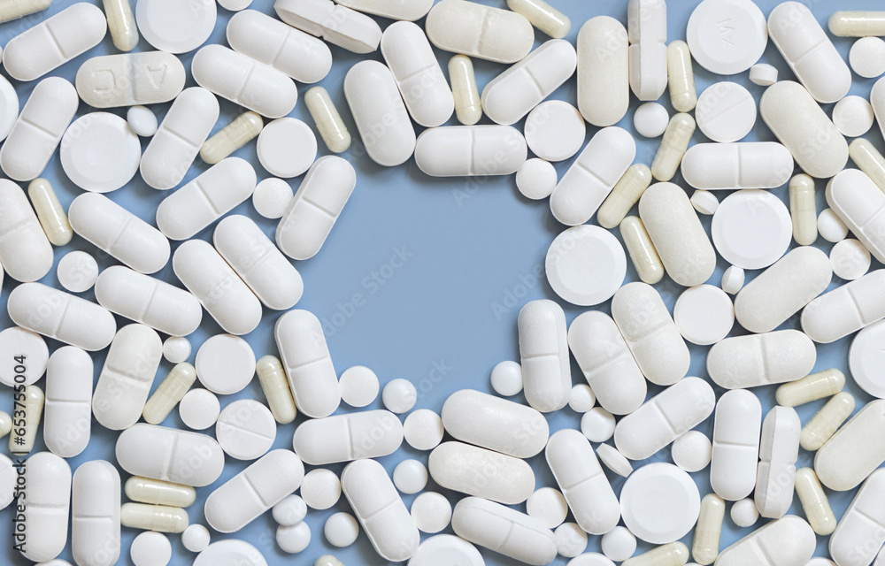Mix of white medical capsules and pills with copy space in the middle on light blue top view Mix of white medical capsules and pills with copy space in the middle on light blue top view
