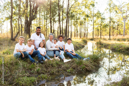 Portrait of happy aboriginal family with lots of children sitting by creek in country