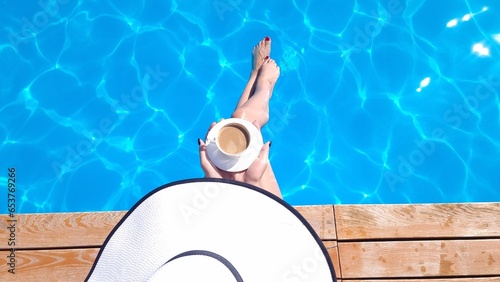 A girl in a hat sits near the pool with a cup of coffee © viktoriya