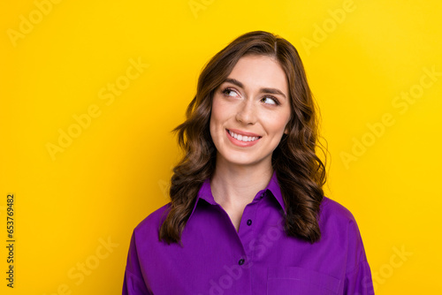 Photo of friendly dreamy satisfied woman with wavy hairstyle dressed purple shirt look at offer empty space isolated on yellow background