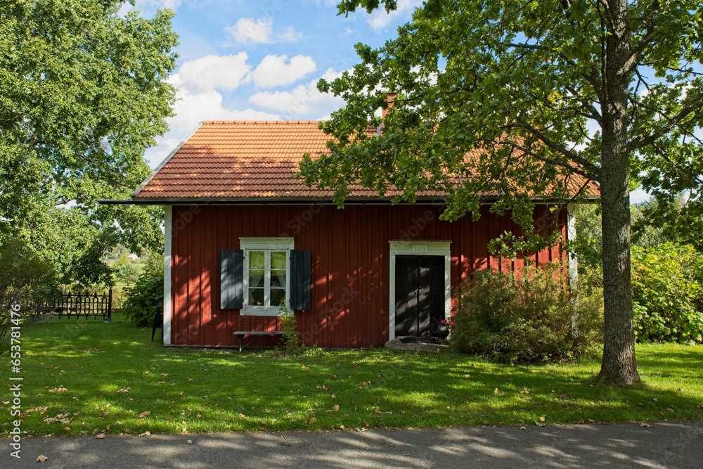 Red painted wooden house and trees in summer.