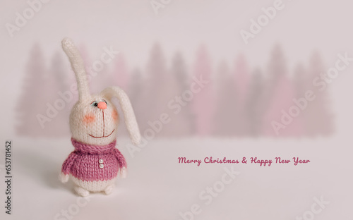 Wallpaper Mural Handmade knitted bunnies stand against a white background. Behind is a forest of fir trees. Postcard for congratulations on the New Year and Christmas holiday. Torontodigital.ca