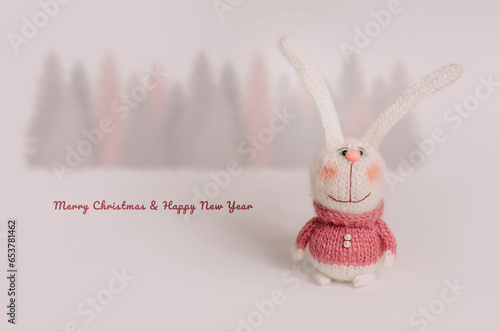 Wallpaper Mural Handmade knitted bunnies stand against a white background. Behind is a forest of fir trees. Postcard for congratulations on the New Year and Christmas holiday. Torontodigital.ca