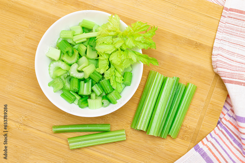 Fresh Chopped Celery Slices in White Bowl with Celery Sticks on Bamboo Cutting Board. Vegan and Vegetarian Culture. Raw Food. Healthy Diet with Negative Calorie Content Fresh Chopped Celery Slices in White Bowl with Celery Sticks on Bamboo Cutting Board. Vegan and Vegetarian Culture. Raw Food. Healthy Diet with Negative Calorie Content